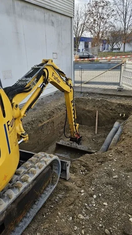 Gelber Minibagger hebt ein Fundament aus und legt Leitungen frei